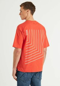 T-shirt in cotone rosso con maniche corte e un design geometrico bianco sulla schiena. Logo 'CHASINI' stampato sulla parte superiore della schiena.