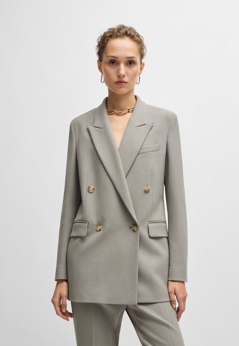 Grå dobbeltradet blazer med klapkraver, struktureret stof, forlommer og store beige knapper.