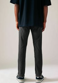 Jeans din denim gri cu o croială dreaptă, asortați cu un tricou scurt și închis la culoare. Tesătura are o textură netedă și detalii de cusătură minime.