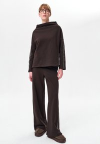 Brązowy zestaw do wypoczynku składający się z topu z szerokim dekoltem z siateczkowymi akcentami na rękawach oraz dopasowanych, luźnych spodni z bocznymi detalami. Miękka faktura.