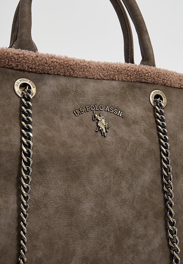 Sac à main en faux suède marron avec un dessus texturé, des accents en doré et une poignée en chaîne. Présente le logo U.S. Polo Assn. à l'avant.