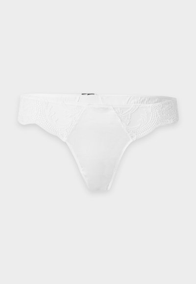 String blanc pour femme avec motif en dentelle sur la taille, panneau avant en tissu lisse, présenté sur un fond clair uni.