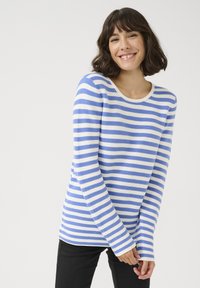 Chemise à manches longues rayée bleue et blanche avec un col rond, présentant un tissu texturé et une coupe ajustée. Associée à un pantalon sombre.