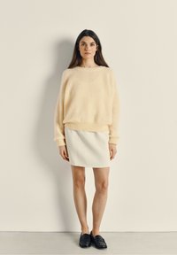 Pull en peluche jaune pâle avec des poignets et un ourlet côtelés, associé à une mini-jupe blanche. Des mocassins noirs complètent le look. Design simple et moderne.