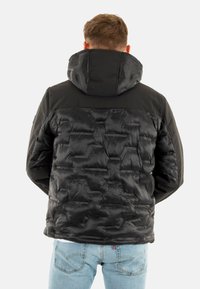 Chaqueta acolchada negra con un patrón de acolchado hexagonal, que presenta un cuello alto y capucha. El material parece brillante y suave; el diseño es aerodinámico.