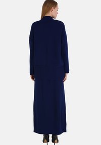 Lungo vestito di maglia blu navy e maglione oversize abbinato, con scollatura rotonda e maniche lunghe, indossato sopra una silhouette elegante.