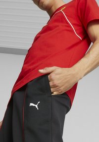 Červené atletické tričko s bílým lemem, doplněné o černé tepláky se bílým logem Puma, vyzdvihující prodyšné materiály a sportovní design.