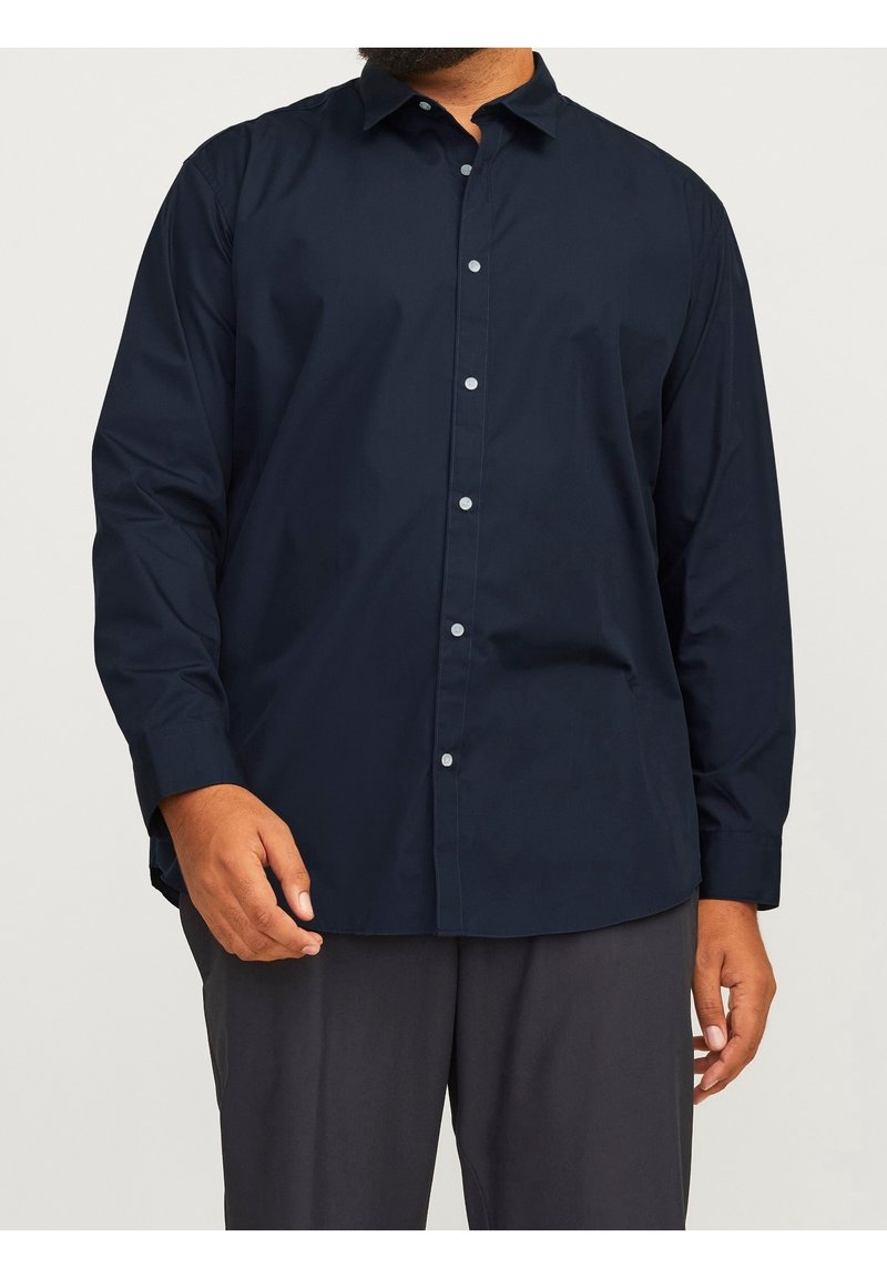 Granatowa, długorękawowa koszula zapinana na guziki z kołnierzykiem i gładką fakturą, zestawiona z ciemnoszarymi spodniami.