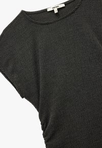 Camiseta negra con textura, de cuello redondo y mangas cortas, con sutiles fruncidos en un lado. Fabricada con material ligero.