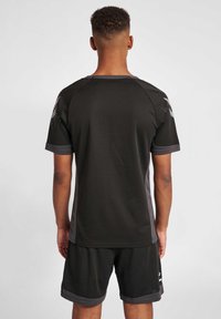 Zwart sportshirt met een gestructureerde afwerking, voorzien van grijze schouderaccenten en logodetails. Gepaard met zwarte shorts, beide gemaakt van lichtgewicht materiaal.