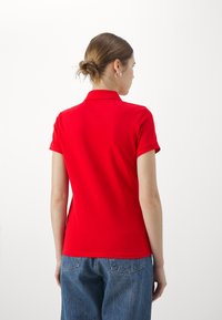 Camisa polo roja de manga corta, con un cuello clásico. Combinada con jeans de mezclilla azul holgados, que presentan un diseño simple y limpio.
