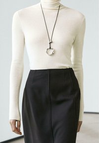 Long-sleeve cream turtleneck top paired with a high-waisted black skirt. A textured silver pendant necklace hangs from a black cord.