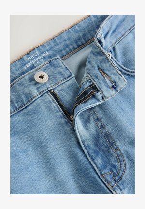 Lyseblå denim-bukser med lynlås, der har kontrastsyninger, en rund metalknap og en glat overflade.