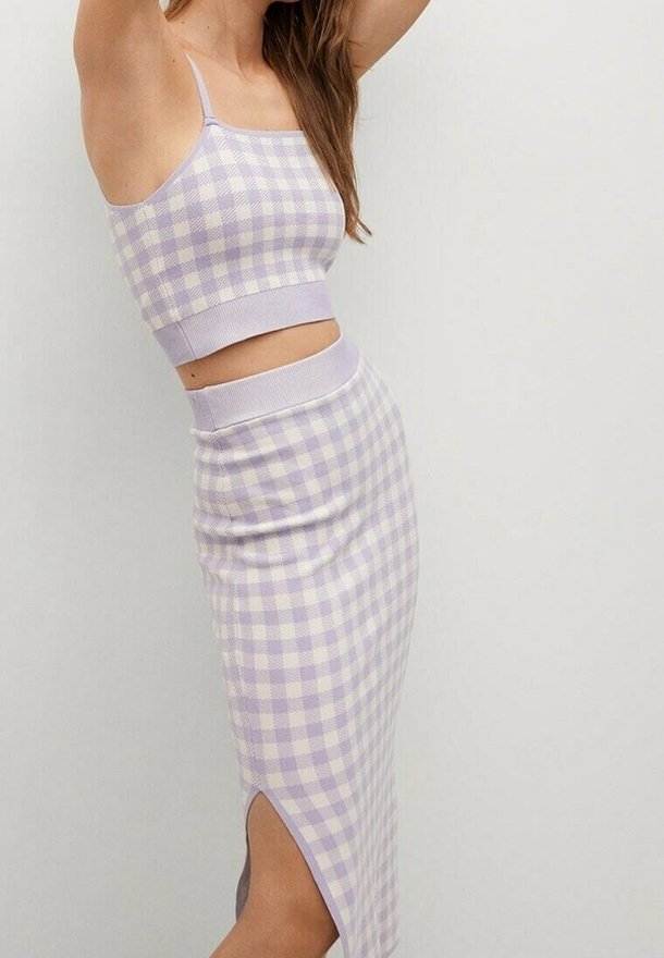 Femme portant une tenue ajustée deux pièces à carreaux lavande et blanc, avec un crop top et une jupe crayon taille haute fendue sur le côté.