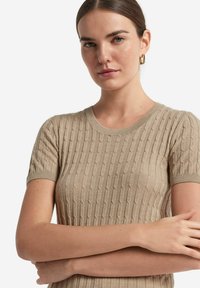 Beige Kurzarmpullover mit geripptem Struktur und vertikalen Mustern sowie einem Rundhalsausschnitt. Glattes Material und taillierte Passform.