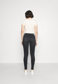 Jeans skinny de mezclilla oscura de cintura alta con un acabado suave, con un diseño de bolsillo trasero y una etiqueta de logo en la cinturilla.