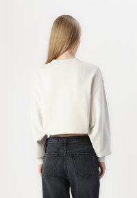 Cropped sweatshirt in off-white fabric with ribbed neckline and dropped shoulders, paired with dark gray denim jeans featuring back pockets.