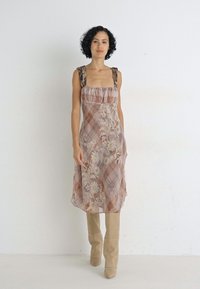 Abito a fantasia floreale nei toni del rosa chiaro e beige, con dettagli a quadri, scollo arricciato e spalline spesse, abbinato a stivali beige al ginocchio.