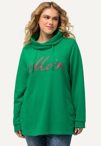 Sudadera verde con cuello tipo embudo, que presenta una gran impresión en script rosa. El material parece suave, con mangas largas y un corte relajado.