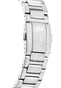 Sidabrinė nerūdijančio plieno laikrodžio apyrankė su brukštiniu paviršiumi, turinti stačiakampius jungiamuosius elementus ir sagtį su antspauduotu logotipu.