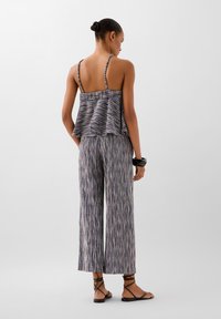 Donna che indossa un top senza maniche a strisce multicolori con spalline sottili e pantaloni a palazzo abbinati, bracciale nero e sandali bassi.