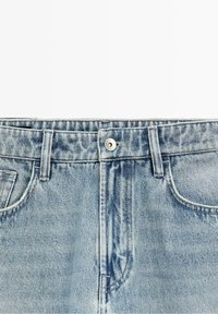 Jean en denim bleu clair avec fermeture à boutons à l'avant, passants de ceinture et poches avant visibles sur fond blanc.