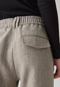 Pantaloni herringbone grigi con vita elasticizzata, cuciture laterali e una singola tasca posteriore. Tessuto testurizzato con un motivo sottile.