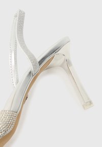 Sølv høyhælte sandaler med en elegant syntetisk overdel, teksturert stropp, åpen tå-design og en blank stiletthæl. Dekorert med rhinestones.
