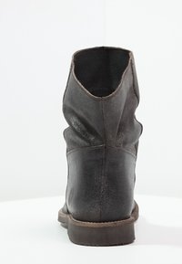 Botte cheville en cuir noir avec un design froissé, une surface texturée et une semelle plate. Coutures visibles et un logo subtil sur le talon.