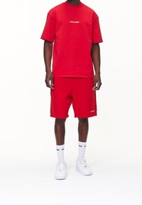 Punainen puuvillainen t-paita ja shortsit, joissa valkoinen "PEGADOR"-logo. Mukana valkoiset sukat ja lenkkarit. Yksinkertainen muotoilu ja rento istuvuus.