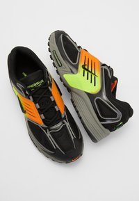 Černé sportovní boty s síťovinou a syntetickými materiály. Obsahují živé oranžové a neonově zelené akcenty, texturované povrchy a robustní podrážku.