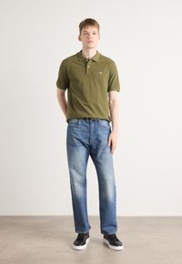 Oliven grøn polo skjorte, denim jeans med lys vask, sorte sneakers med hvide såler. Casual fit, glat tekstur, kortærmede.
