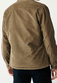 Braune Cordjacke mit einer strukturierten Oberfläche, Knopfmanschetten und geradem Schnitt. Ausgestattet mit einem klassischen Kragen und einer Schulterpasse am Rücken.