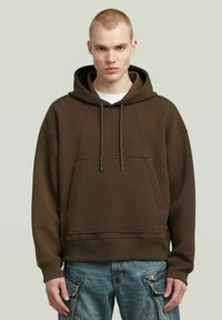 Bruine pullover hoodie met een kangoeroezak, een capuchon met trekkoord en geribde manchetten. Gedragen over een wit shirt, gecombineerd met blauwe cargobroek.