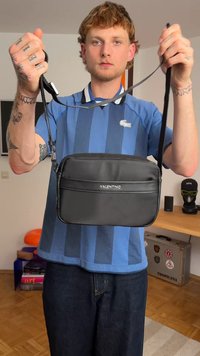 Bolsa preta da Valentino com textura lisa e mate e logo prateado. Apresenta um formato retangular e uma alça ajustável.