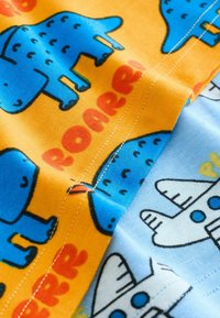 Zbliżenie tkaniny z niebieskimi ilustracjami dinozaurów oraz czerwonym napisem „ROAR” na pomarańczowym tle, obok biały nadruk samolotów na jasnoniebieskiej tkaninie.