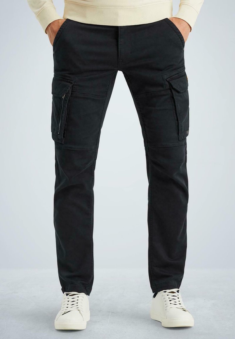 Schwarze Cargo-Hosen mit vorderen und seitlichen Taschen, aus robustem Stoff; Slim-Fit-Design; kombiniert mit weißen Sneakern auf einem hellen Hintergrund.