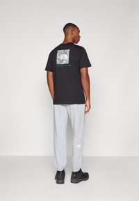 Sort bomulds t-shirt med et grafisk print på ryggen, parret med grå sweatpants, der har elastiske manchetter og et logo nær anklen.