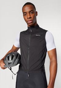 Zwart mouwloos fietsvest met een hoge kraag, ritssluiting en gripGrab-logo, gedragen over een wit T-shirt met korte mouwen. Grijze helm in de hand.