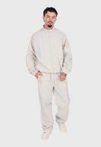 Tuta grigio chiaro composto da una giacca con zip e polsini elasticizzati, abbinata a pantaloni, entrambi realizzati in un tessuto liscio con una vestibilità comoda.