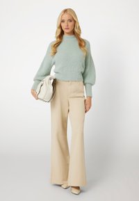 Mėtų žalios spalvos pūkuota megzta palaidinė su burbulinėmis rankovėmis, smėlio spalvos plačių kojų kelnės ir balta rankinė. Avalynė - šviesios spalvos smailiakulniai bateliai.