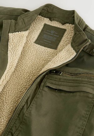 Olive green jacket with a soft, cream-colored sherpa lining. Features a zip closure and one exterior pocket with a zip and two interior pockets.
