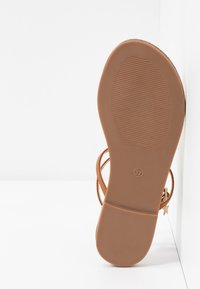 Semelle plate de sandale marron marquée taille 37, présentée debout contre un fond blanc en angle.