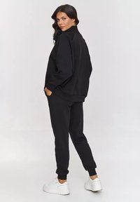 Czarna bluza i dresy wykonane z miękkiego materiału, z luźnym krojem, ściągaczami u mankietów i bocznymi kieszeniami. W zestawie z białymi sneakersami.