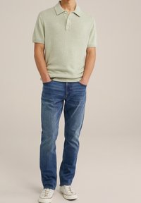 Ljusgrön stickad pikétröja med krage, korta ärmar och tre knappar, matchad med blå jeans och vita sneakers.