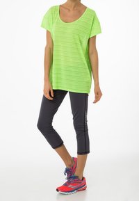 Neon grön randig kortärmad t-shirt i kombination med mörka cropped träningsbyxor och rosa löparskor med blå detaljer.