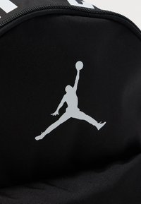 Μαύρη υφασμάτινη επιφάνεια με μια λευκή σιλουέτα καλαθοσφαιριστή που πηδάει και τεντώνει το ένα χέρι κρατώντας μια μπάλα.