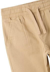 Pantaloni beige con elastico in vita e stringa, dotati di due tasche laterali e una texture liscia. Design casual con una vestibilità comoda.