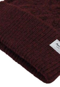 Burgundy neulepipo, jossa on ribbitettu rakenne, taitettu reunus ja pieni valkoinen etiketti, jossa on mustaa tekstiä sivussa.