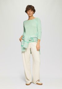 Licht muntgroene langemouwen top met een relaxed fit, gecombineerd met crèmekleurige wijde broek en beige sneakers. Sweater om de taille geknoopt.